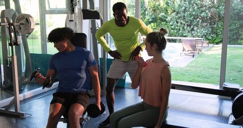 Young Couple Exercising in Gym with Trainer Supervising