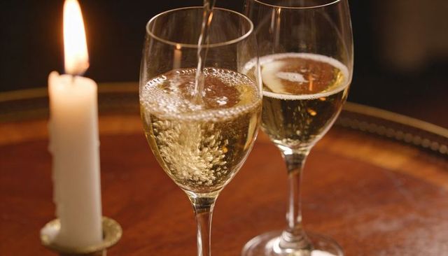 Pouring sparkling wine into glasses by candlelight for intimate romantic celebration dinner