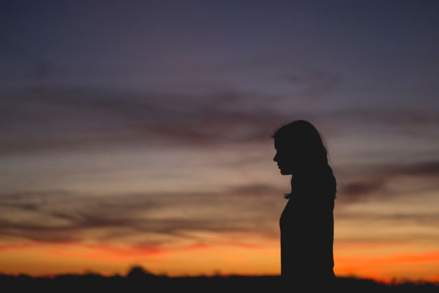 Woman silhouetted against twilight sky, perfect for themes of peace, contemplation, and solitude. Suitable for use in articles or content related to introspection, mental health, or tranquility.