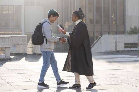 Two diverse male friends celebrating college graduation on campus, graduate shaking hands