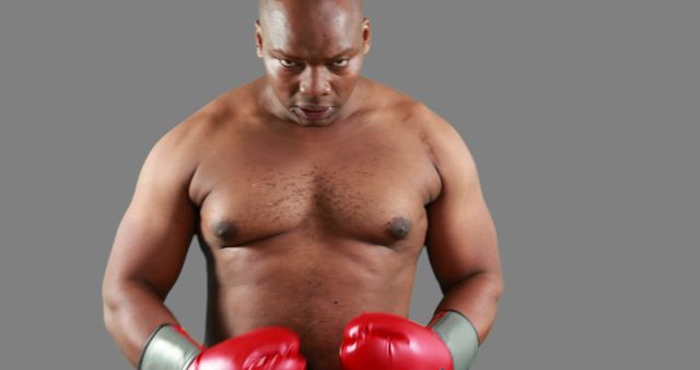A shirtless boxer with a determined expression wearing red gloves and staring straight ahead. Ideal for sports, fitness, athleticism, and motivation themes.