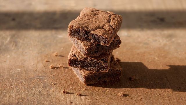 Stacking fudgy chocolate brownies on rustic wooden board with warm sunlight and crumb texture