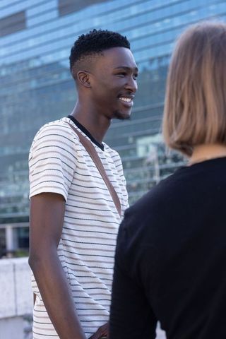 Young man and woman chatting near glass office building smiling in candid urban conversation dayligh