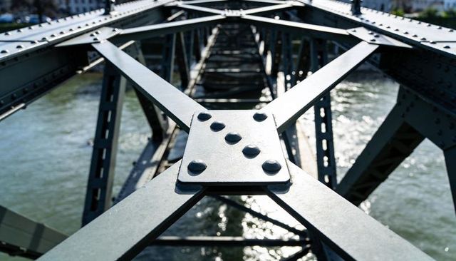 Close-up bolted steel truss bridge revealing rivets and diagonal beams over river