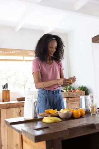 African american woman peeling oranges in bright rustic kitchen preparing fresh fruit