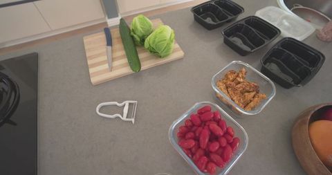 Meal prepping on modern kitchen countertop with glass containers, cherry tomatoes, chicken