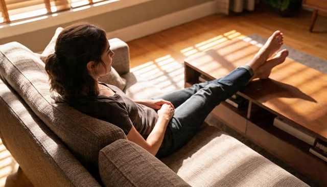 Sunlit woman reclining on sofa with legs on coffee table relaxing in cozy living space