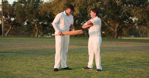 Coach demonstrating batting technique to teammate during outdoor cricket training session