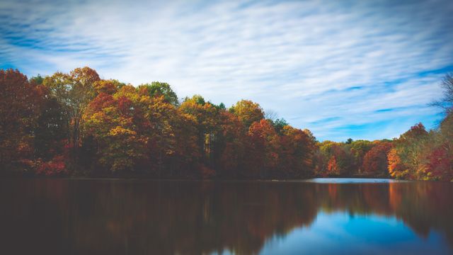 Scenic autumn landscape featuring a calm lake surrounded by colorful foliage with reflections on water. Suitable for nature-themed projects, travel brochures, or seasonal publications highlighting the beauty of autumn.