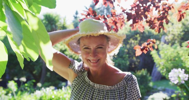 Portrait of happy caucasian senior woman walking in garden wearing sunhat and smiling in the sun. staying at home in isolation during quarantine lockdown.