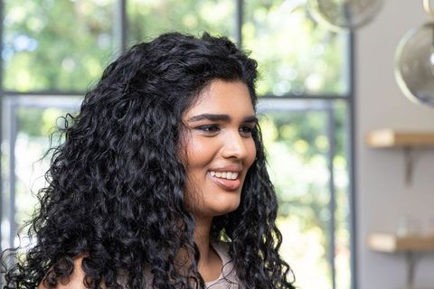 Smiling young woman with curly hair sitting by multipane window in modern bright interior