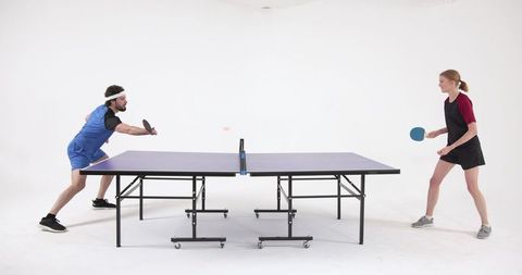 Diverse duo engaged in energetic ping pong match indoors