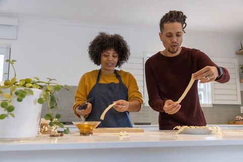 Couple baking lattice pie together wearing knit sweaters in bright home kitchen
