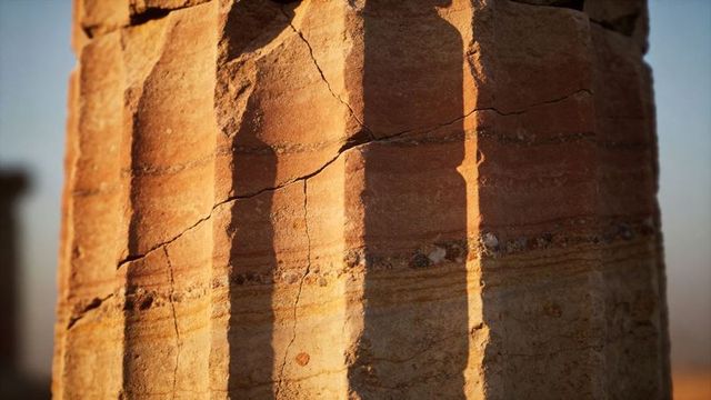 Sunlit weathered sandstone column with fluted grooves and deep shadows at ruin, textured pebbles