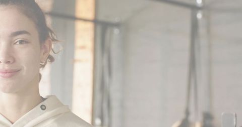 Smiling young woman wearing light hoodie standing in industrial gym with rig and ropes