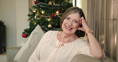 Smiling Senior Woman Relaxing by Christmas Tree in Cozy Living Room