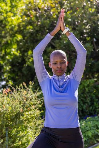 African woman practicing outdoor yoga in sunlit garden wearing purple top and smartwatch