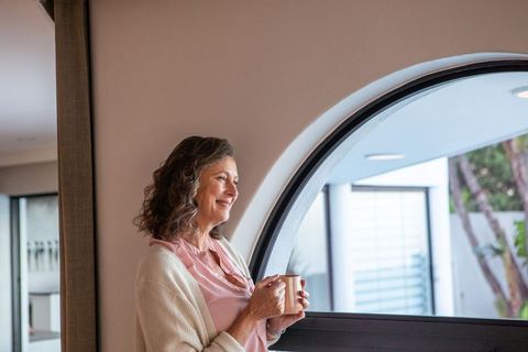 Senior Woman Enjoying Coffee by Arched Window in Cozy Living Room