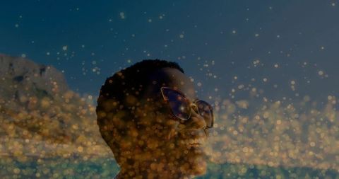 Gazing woman wearing oversized reflective sunglasses facing sunlit ocean with golden bokeh