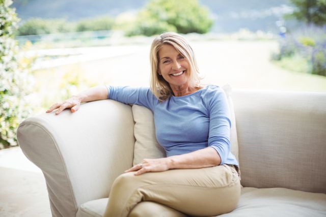Portrait of smiling senior woman sitting on sofa in living room at home