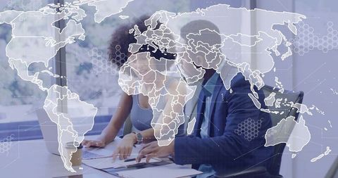 Business team collaborating over laptop and documents with world map analytics overlay