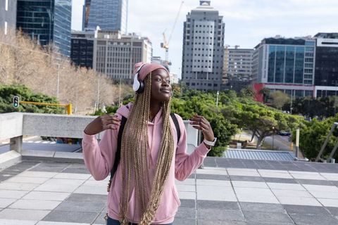 African American Woman Listening to Headphones in Pink Hoodie Enjoying City Morning