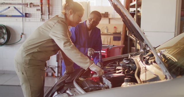This image shows a male and female mechanic working together on a car engine in a garage. It is ideal for use in marketing materials for automotive repair shops, articles about gender diversity in technical fields, educational content for automotive repair training, or promoting teamwork and technical skills in working environments.
