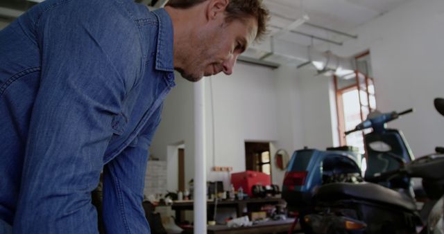 Mechanic focusing on repairing a scooter in an urban garage workshop filled with various tools and parts. Ideal for illustrating mechanical maintenance, professional repair services, and technical garage environments.