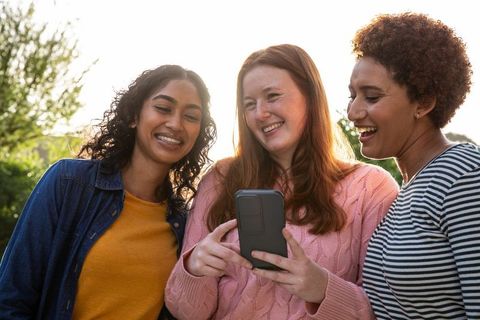 Diverse female friends smiling and sharing moments on smartphone