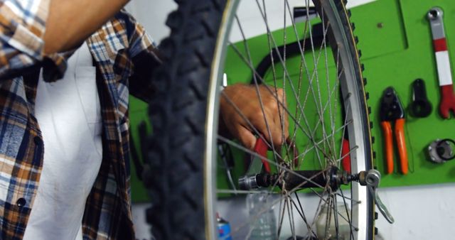 Man repairing bicycle tire in workshop, showing detailed work with tools hanging on wall. Ideal for illustrating bike maintenance, DIY repair guides, or mechanic services.