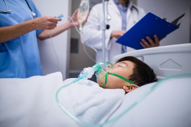 This image depicts doctors adjusting an IV drip for a young patient lying in a hospital bed with an oxygen mask. It is ideal for use in healthcare-related articles, medical websites, pediatric care promotions, and educational materials about hospital procedures and patient care.