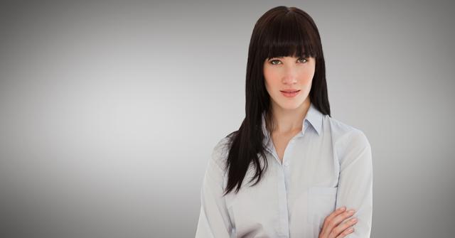 Confident businesswoman standing with arms crossed against grey background