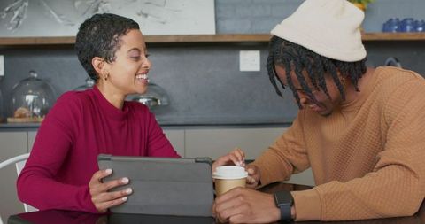 Smiling multiracial friends sharing tablet and coffee while chatting in cozy coffeehouse