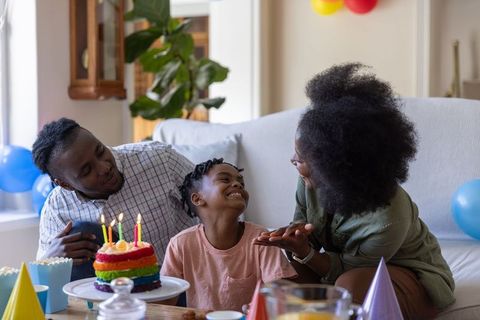 African american family celebrating birthday with rainbow cake and candles in living room