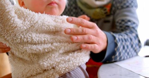 Father Helping Young Daughter Put On Sweater at Home
