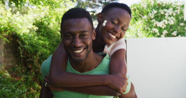 Happy african american couple having fun piggybacking in sunny garden and smiling. staying at home in isolation during quarantine lockdown.
