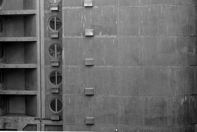 This stock photo features an abstract view of urban architecture, showcasing a modern building with geometric shapes and textured concrete surfaces. Circular windows and rectangular elements add to the structural creativity. Suitable for use in architectural journals, websites, and marketing materials that focus on modern design aesthetics or urban living.