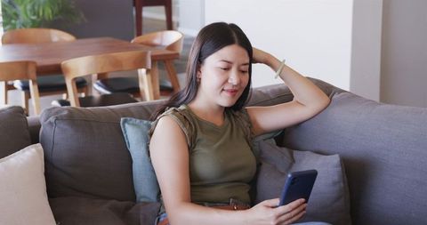 Young woman relaxing on sofa scrolling smartphone in cozy minimalist living room