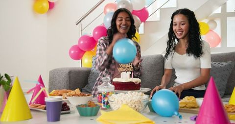 Women celebrating birthday with cake and balloons at home party