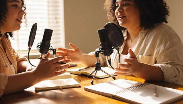 Sunlit conversational podcast recording with two co-hosts, microphones, notebooks, creative collabor