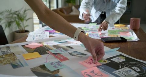 Diverse team brainstorming at home office arranging colorful sticky notes on moodboard
