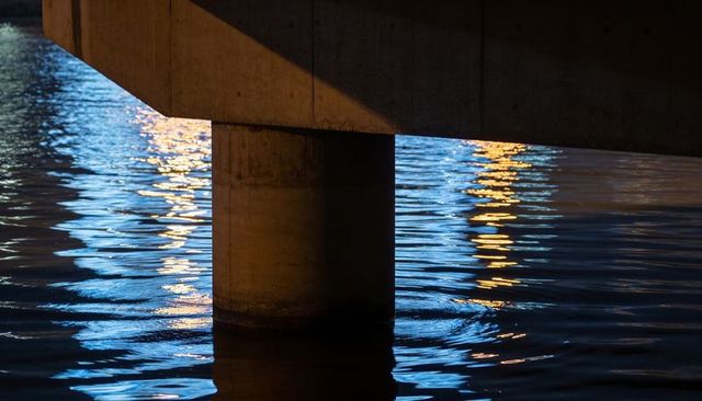 Glowing Blue and Orange Water Reflections around Concrete Bridge Column at Night