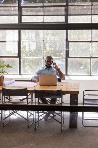 Businessman Discussing While Checking Content on Laptop and Blueprint Desk
