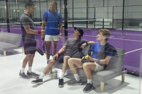 Diverse men chatting and relaxing courtside at indoor paddle court with purple turf