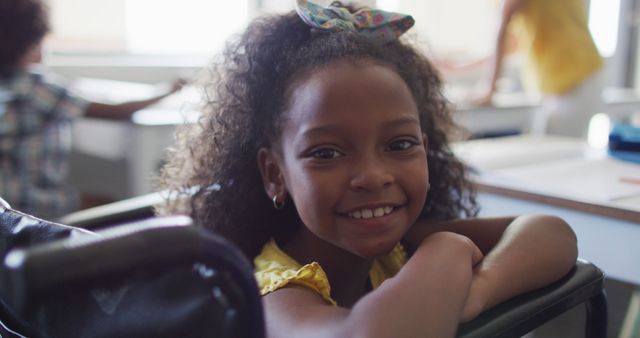 Image of happy disabled african american girl sitting at desk in classroom. disability, primary school education and learning concept.