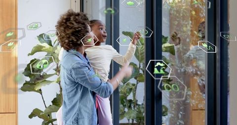 Woman holding child pointing at augmented reality interface on modern lobby glass