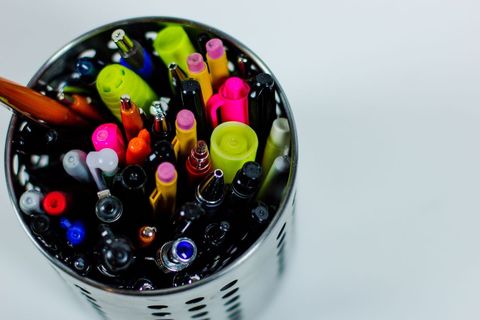 Diverse collection of colored pens in metallic holder on desk