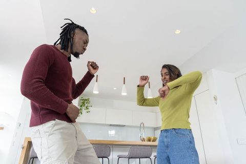 African american man and indian woman dancing in modern kitchen wearing sweaters