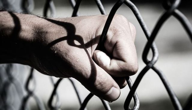 Gripping hand on chain-link fence with shadow and water droplets, closeup emotion