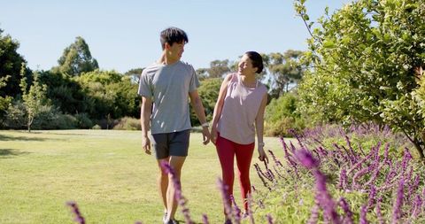 Young couple walking and checking fitness watches in sunlit park with purple flowers